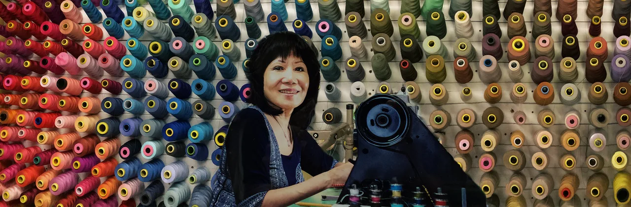 Kim Ho, owner and seamstress, smiling at her sewing machine in the shop