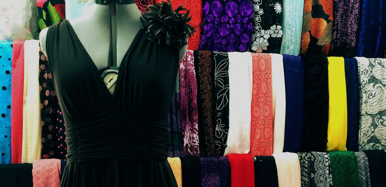 A fitted black dress displayed beside richly patterned fabrics in the tailoring shop